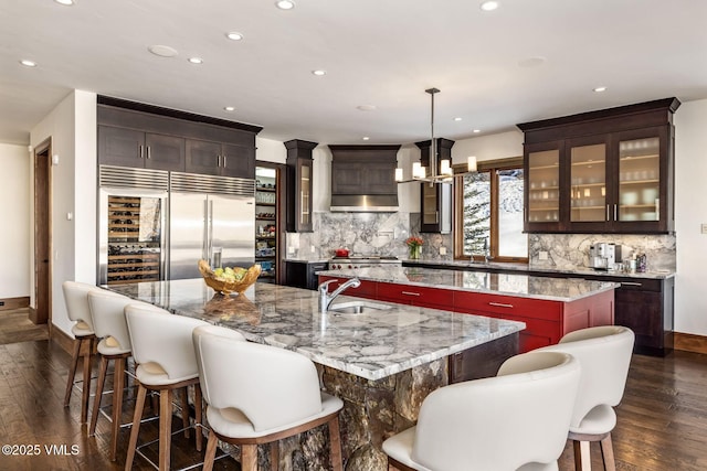 kitchen featuring backsplash, dark hardwood / wood-style floors, light stone counters, decorative light fixtures, and a large island with sink