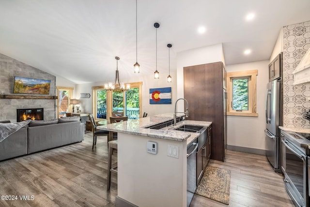 kitchen with sink, vaulted ceiling, appliances with stainless steel finishes, light stone countertops, and a kitchen island with sink