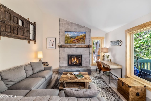 living room with lofted ceiling, a tiled fireplace, hardwood / wood-style floors, and a wealth of natural light