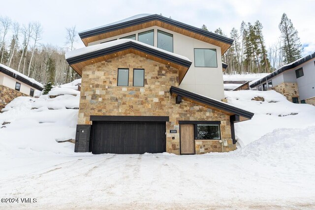 snow covered back of property featuring a garage