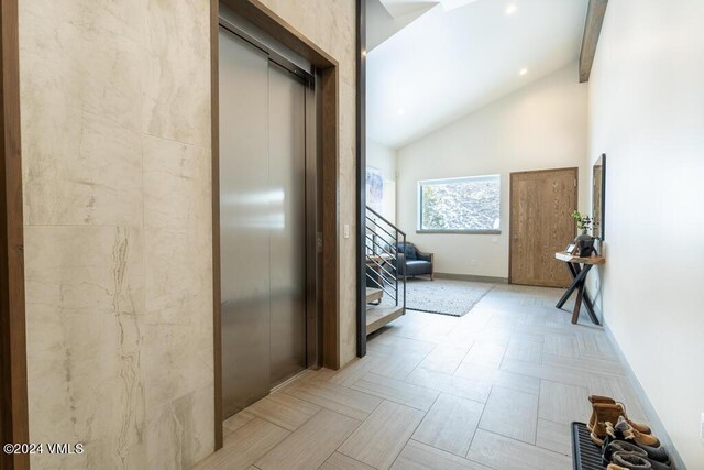 hall with beam ceiling, light parquet floors, high vaulted ceiling, and elevator