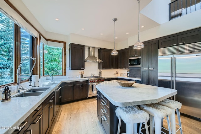 44 Conestoga Cir, Edwards, CO 81632 - kitchen featuring built in appliances, wall chimney range hood, light stone counters, light wood-style flooring, and dark brown cabinetry