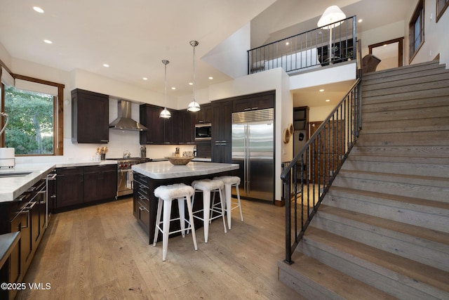 44 Conestoga Cir, Edwards, CO 81632 - kitchen with built in appliances, wall chimney range hood, dark brown cabinetry, a kitchen bar, and a center island