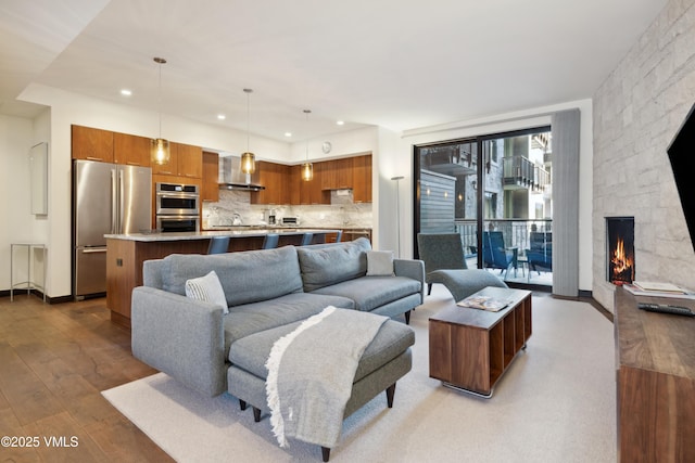 living area with recessed lighting, baseboards, a stone fireplace, and hardwood / wood-style flooring