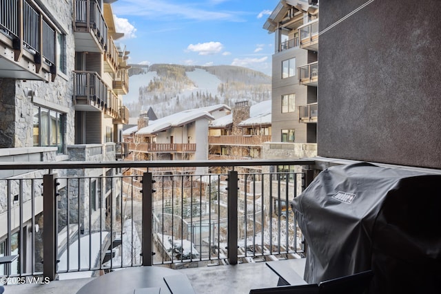 snow covered back of property featuring a mountain view, a residential view, and a grill