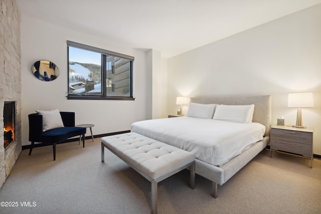 carpeted bedroom featuring a stone fireplace and baseboards