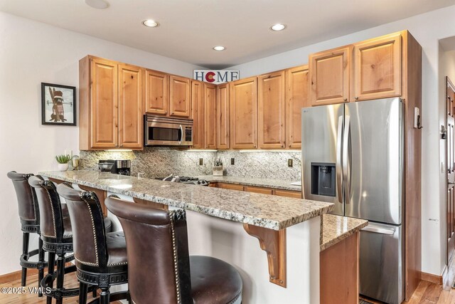 107 Lions Ln, Minturn, CO 81645 - kitchen with a kitchen breakfast bar, light stone counters, a peninsula, backsplash, and appliances with stainless steel finishes