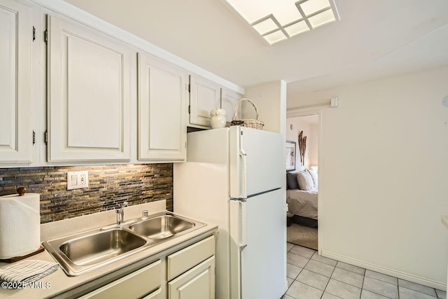 kitchen featuring light tile patterned floors, tasteful backsplash, freestanding refrigerator, white cabinetry, and a sink