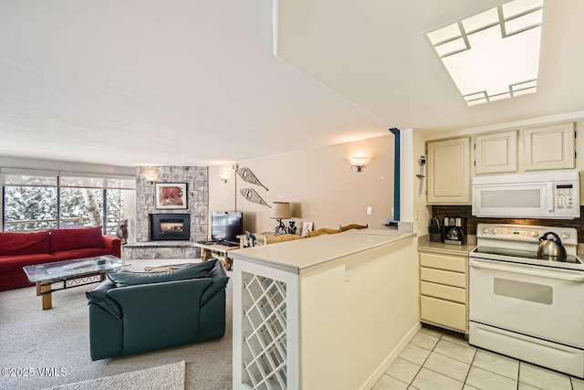 kitchen featuring white appliances, open floor plan, a peninsula, light countertops, and a fireplace