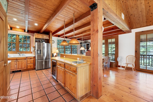 kitchen featuring a sink, light countertops, wine cooler, stainless steel refrigerator with ice dispenser, and beamed ceiling