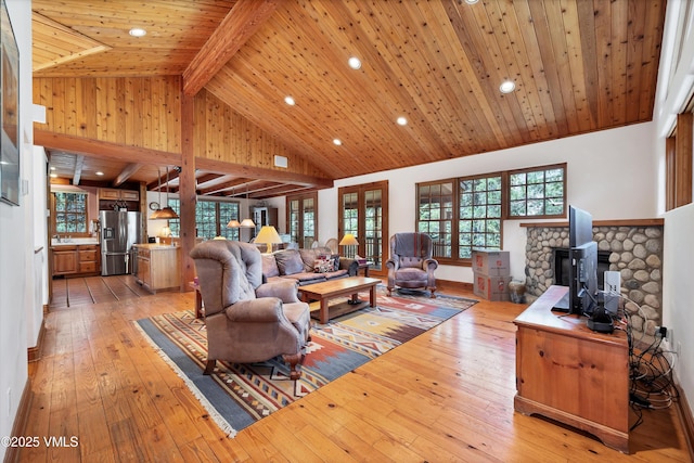 living room with recessed lighting, lofted ceiling with beams, a wood stove, and light wood finished floors