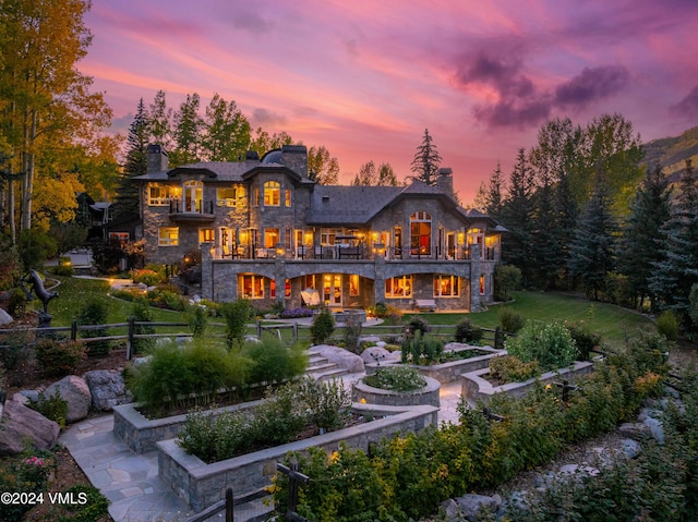 back house at dusk with a balcony and a yard