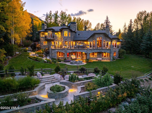 back house at dusk with a patio, a balcony, an outdoor fire pit, and a lawn