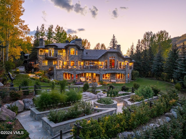 back house at dusk with a lawn and a balcony