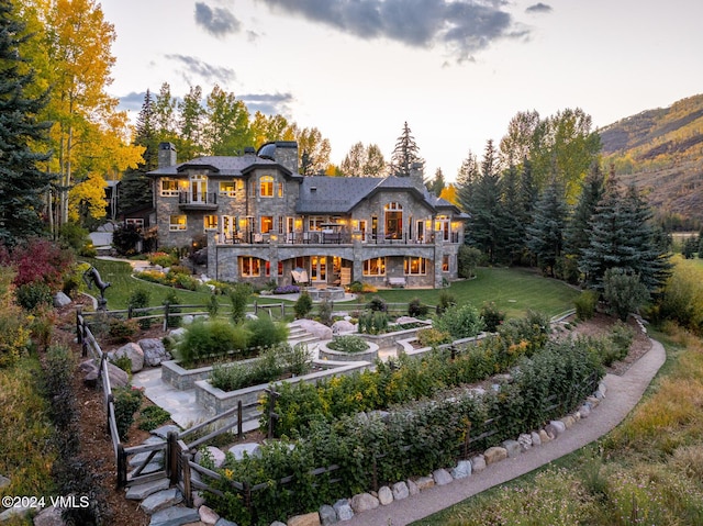 back house at dusk with a balcony and a yard