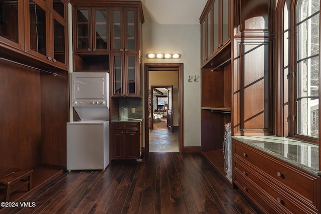 interior space with stacked washer and clothes dryer, dark hardwood / wood-style floors, decorative backsplash, and dark stone counters