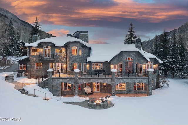 snow covered rear of property featuring a mountain view and a fire pit