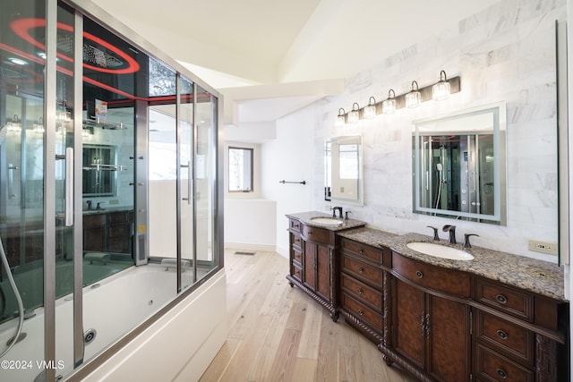 full bathroom with double vanity, enclosed tub / shower combo, a sink, and wood finished floors