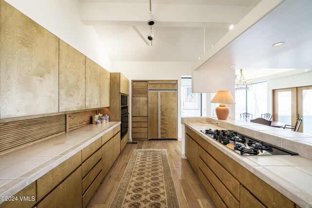 kitchen with brown cabinets, tile counters, light wood-style floors, modern cabinets, and black appliances