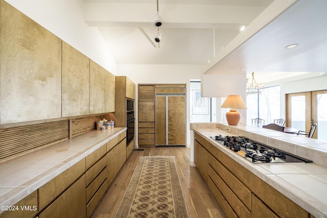 kitchen featuring light wood-style flooring, tile counters, brown cabinets, black appliances, and modern cabinets