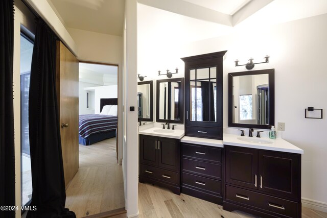 ensuite bathroom with double vanity, wood finished floors, a sink, and connected bathroom