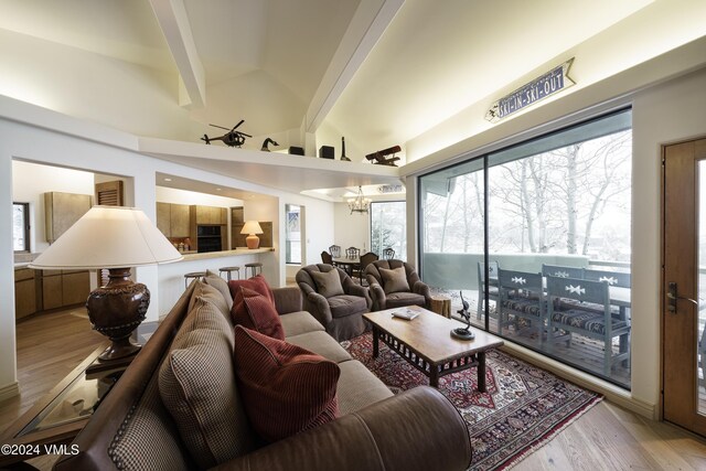 living area featuring lofted ceiling with beams, light wood-style floors, and a notable chandelier