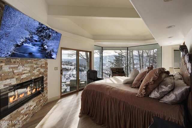 bedroom with a glass covered fireplace, wood finished floors, access to exterior, vaulted ceiling, and a mountain view