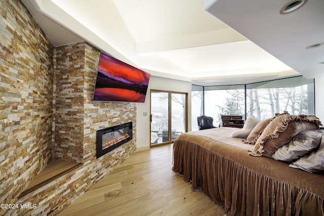 bedroom featuring access to outside, a glass covered fireplace, and light wood-style floors