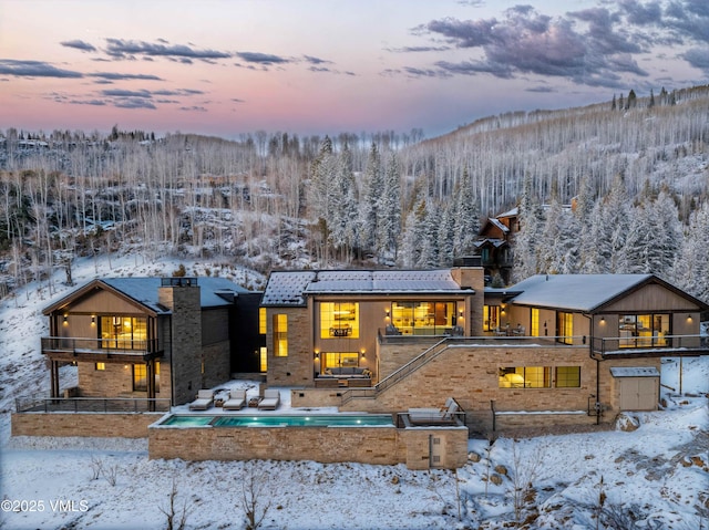 snow covered property featuring a balcony, a chimney, and a mountain view