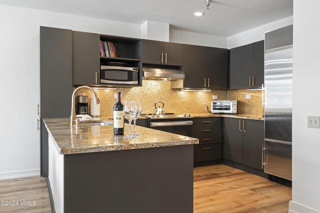 kitchen with light stone counters, stainless steel appliances, range hood, and sink