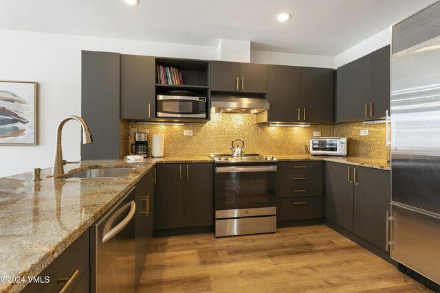 kitchen featuring sink, stainless steel appliances, light stone counters, ventilation hood, and light wood-type flooring