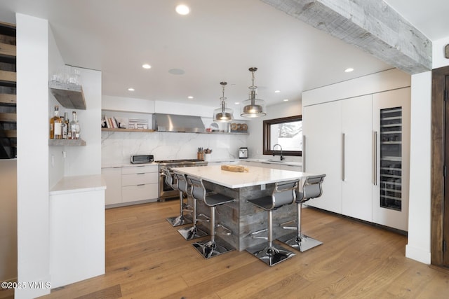 kitchen featuring wall chimney range hood, gas range, paneled built in fridge, a kitchen breakfast bar, and a sink