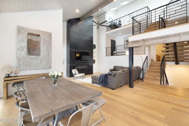 dining area with a ceiling fan, wood finished floors, stairway, a large fireplace, and a high ceiling