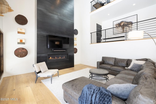 living area featuring baseboards, a large fireplace, wood finished floors, and a towering ceiling