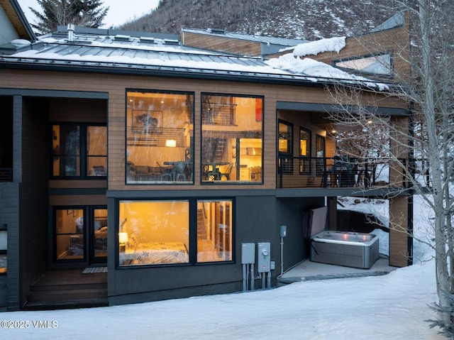 snow covered rear of property featuring a standing seam roof and metal roof