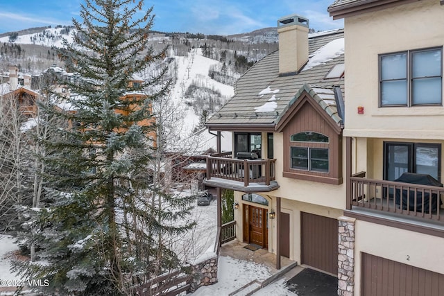 exterior space with stucco siding, a mountain view, a balcony, a chimney, and a tiled roof