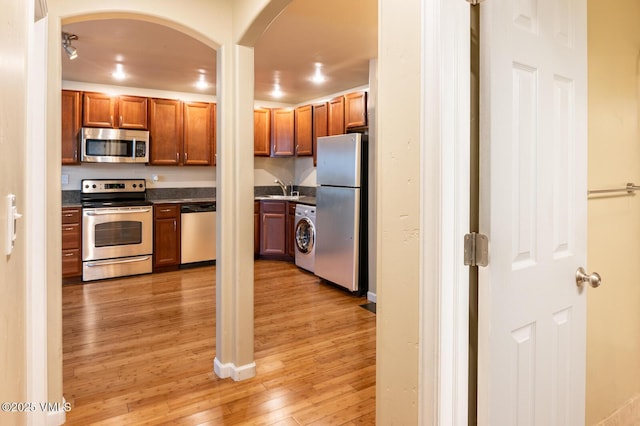 kitchen featuring dark countertops, appliances with stainless steel finishes, light wood-style floors, washer / clothes dryer, and a sink