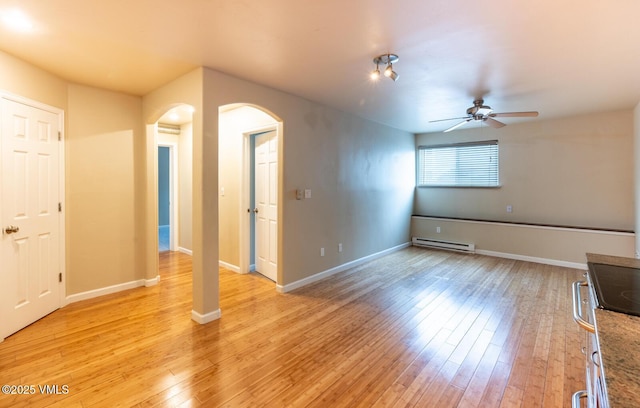 spare room featuring arched walkways, light wood finished floors, baseboards, and a baseboard radiator