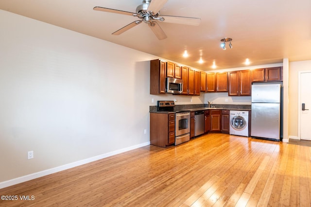 kitchen with dark countertops, light wood-style flooring, appliances with stainless steel finishes, and washer / clothes dryer