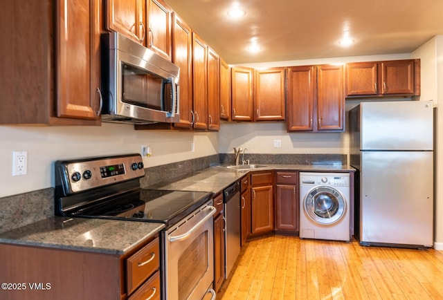 kitchen with light wood-style flooring, appliances with stainless steel finishes, brown cabinetry, washer / clothes dryer, and a sink