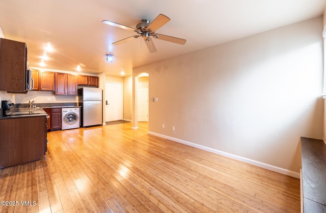 kitchen featuring washer / clothes dryer, dark countertops, stainless steel appliances, arched walkways, and light wood finished floors