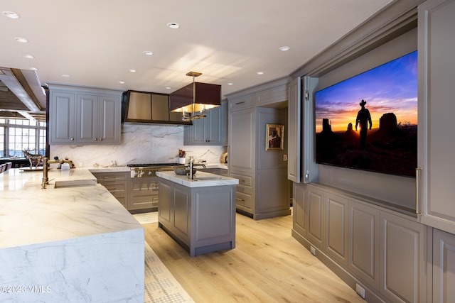 17 Chateau Ln Unit 501, Beaver Creek, CO 81620 - kitchen with gray cabinets, wall chimney range hood, backsplash, an island with sink, and light wood-style floors