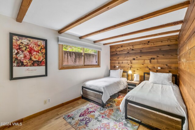 bedroom featuring wooden walls, beam ceiling, and light hardwood / wood-style floors