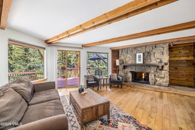 living room featuring hardwood / wood-style floors, a stone fireplace, and beamed ceiling