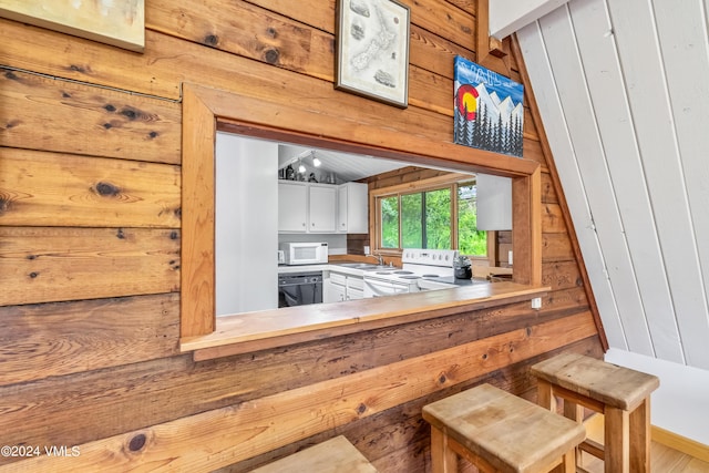 kitchen featuring white appliances, wooden walls, sink, and white cabinets