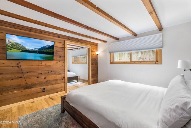 bedroom with wood-type flooring, beamed ceiling, and wood walls