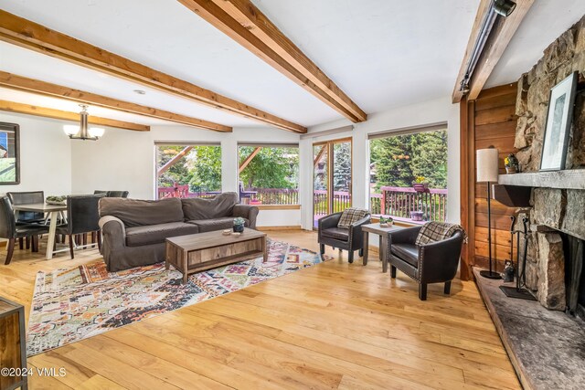 living room featuring beamed ceiling, a stone fireplace, a chandelier, and light wood-type flooring