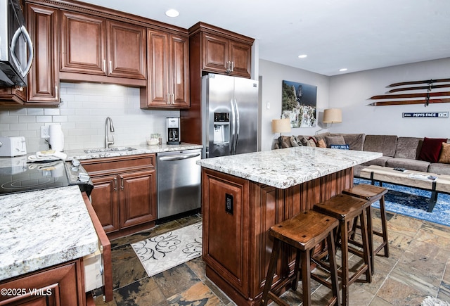 kitchen with stone tile flooring, decorative backsplash, a sink, appliances with stainless steel finishes, and open floor plan