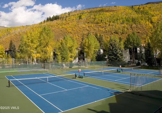 view of sport court featuring a forest view and fence