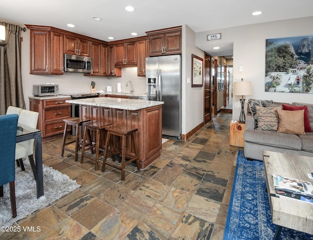 kitchen with a sink, appliances with stainless steel finishes, open floor plan, and stone tile flooring